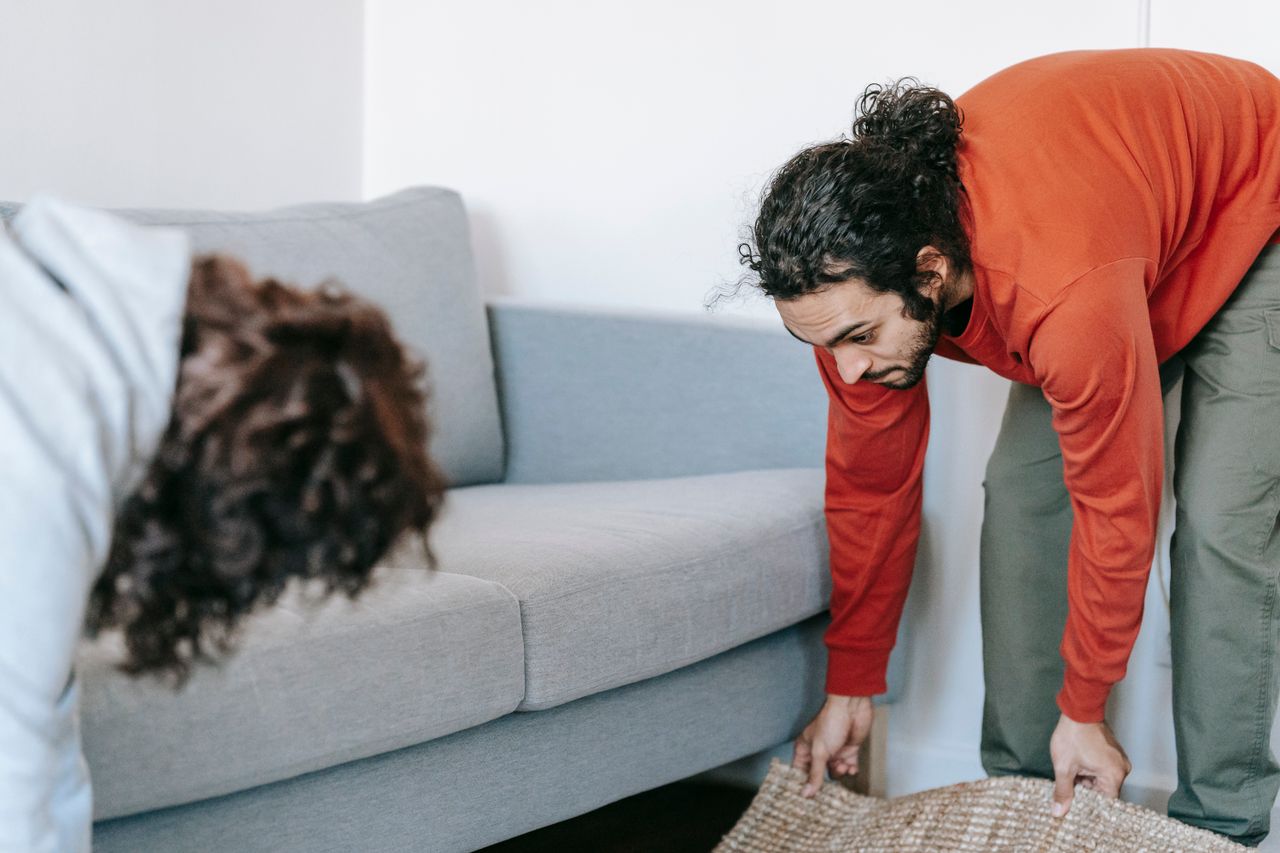 A couple tidying up their living room, organizing furniture and rugs with teamwork.
